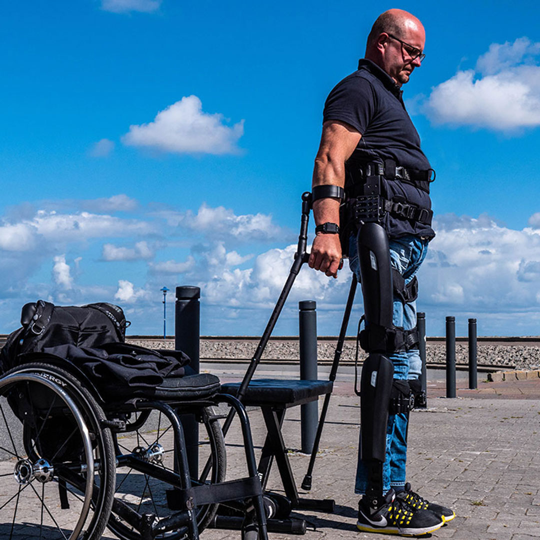 Mann-in-Exoskelett-steht-vor-Rollstuhl
