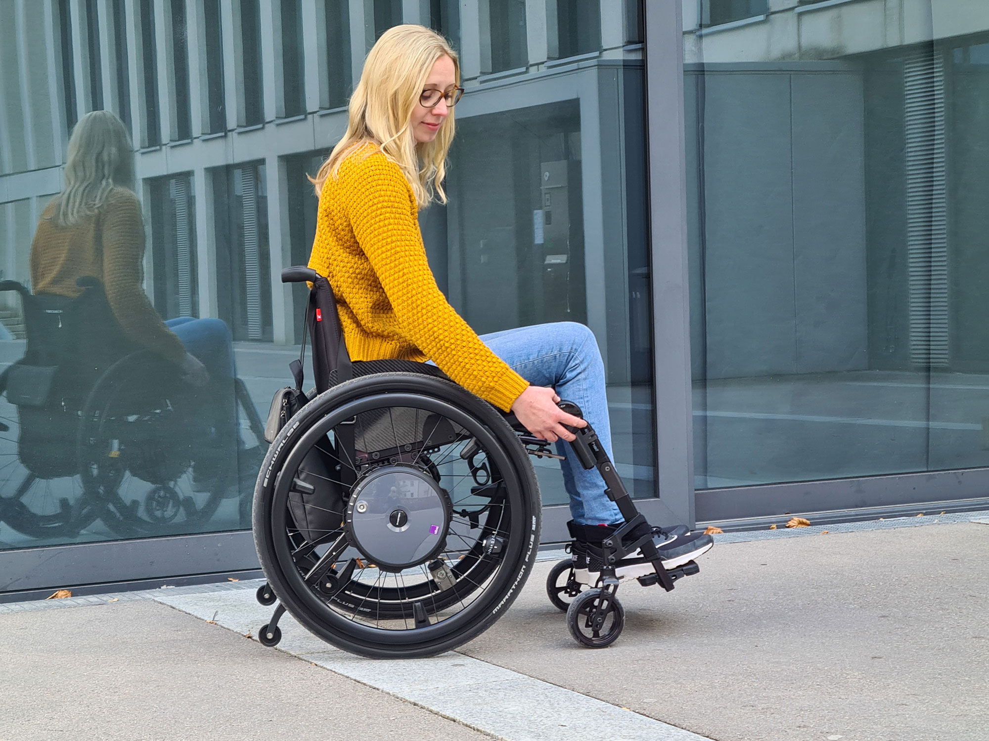 blonde-Frau-mit-Brille-in-Aktiv-Rollstuhl-bedient-Alber-e-motion-DuoDrive-via-Fernbedienung